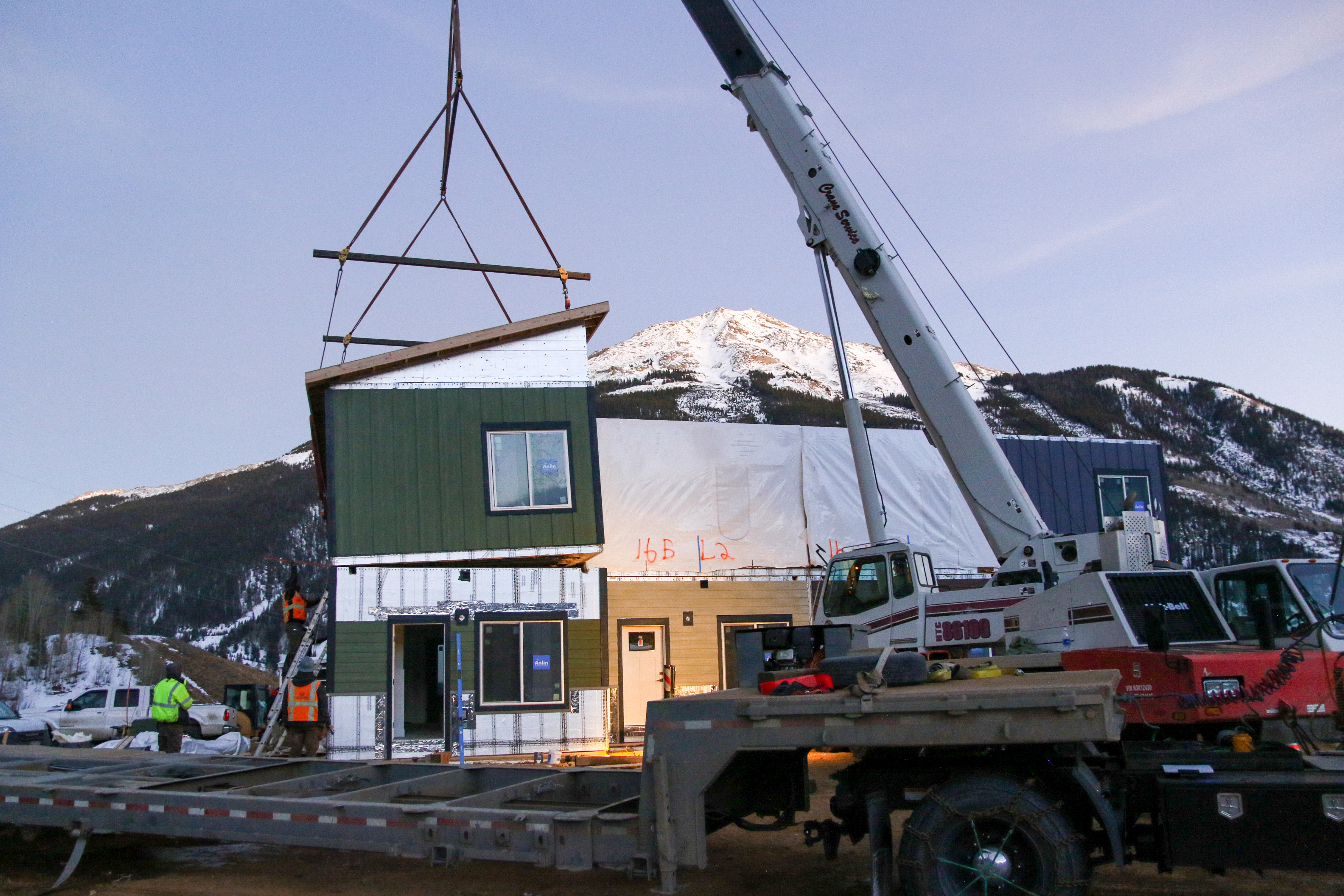 Photo of a crane stacking a modular home on a four-plex with mountains in the background